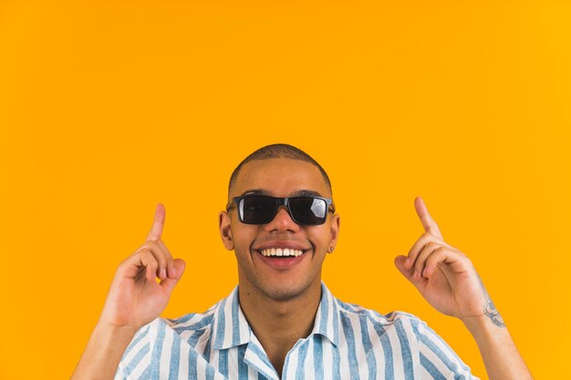 Cheerful afroamerican boy with sunglasses pointing above himself on the yellow background medium