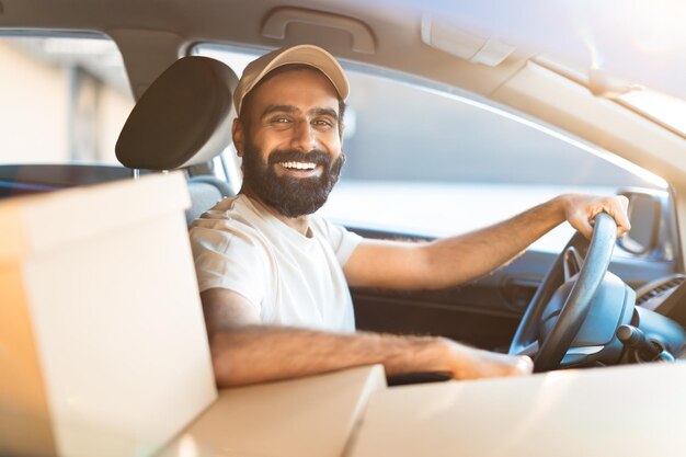 Photo cheerful arab courier guy sitting in automobile with parcels