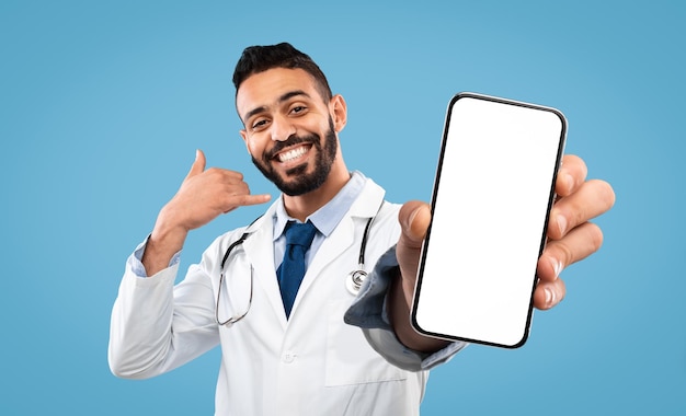 Cheerful arab doctor male gesturing call me holding smartphone