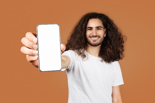 Cheerful arab guy shows big touchscreen phone against beige backdrop