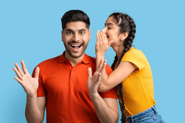 Cheerful arab woman sharing secrets with excited boyfriend whispering to his ear