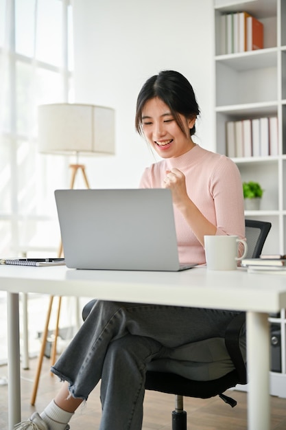 Cheerful Asian businesswoman showing her fist rejoicing after receiving an unexpected email