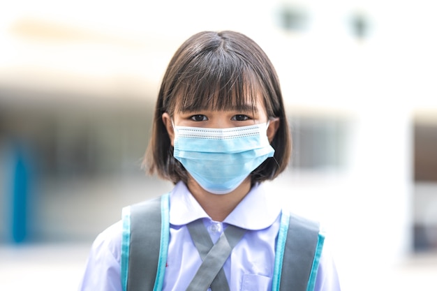COVID-19 전염병 이후 의료용 안면 마스크를 쓰고 학생복을 입은 쾌활한 아시아 어린이 학생. 학교 개념으로 돌아가기 스톡 포토