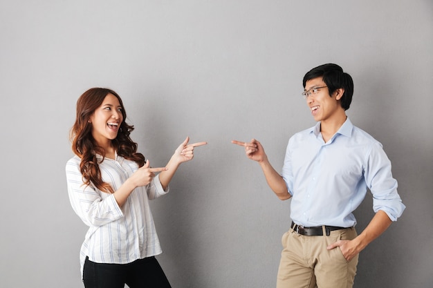 Cheerful asian couple standing isolated, pointing