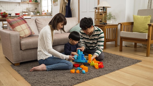 cheerful asian father, mother and baby son having fun playing colorful toy blocks in the living room at home