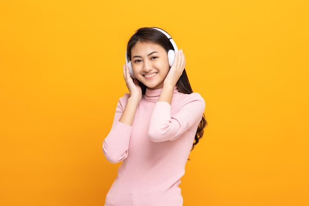 Cheerful asian female teenager listen to the music with white headphone dancing on isolated yellow background Beautiful young woman in hand touch a wireless headphone having fun with music