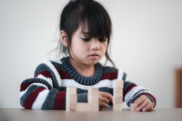 Cheerful Asian girl playing with wooden building blocks. Having fun and learning creativity. smart kid concept.