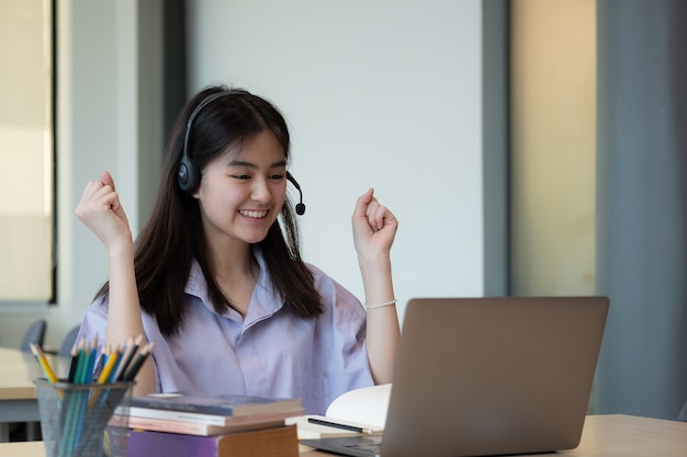 Cheerful asian girl wear wireless headset laughing with laptop