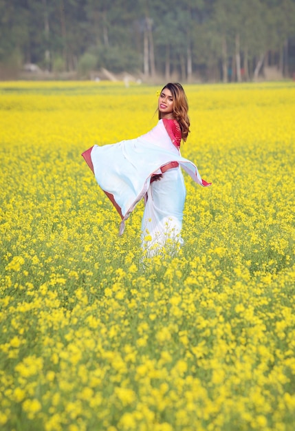 A cheerful Asian girl wearing red blouse and white saree in yellow mustard field