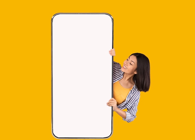 写真 大きな白い空のスマートフォンの画面を示す陽気なアジアの女性