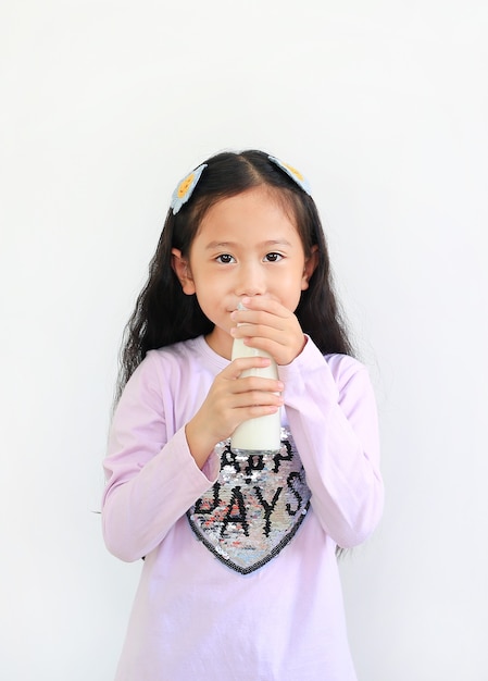 Bambina asiatica allegra che beve latte dalla bottiglia di vetro isolata su fondo bianco.