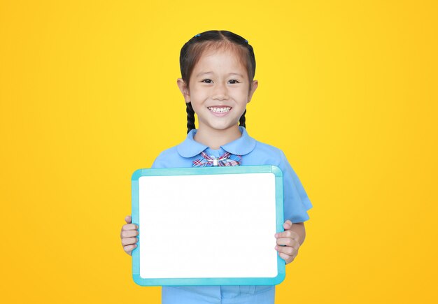 Bambina asiatica allegra in uniforme scolastico che giudica lavagna bianca in bianco isolata. concetto di studente e istruzione.