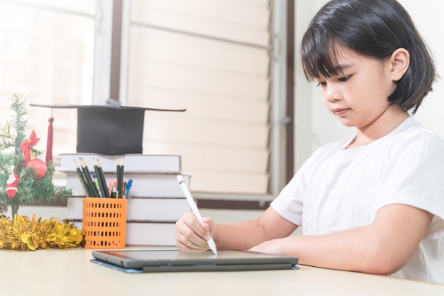 Una studentessa asiatica allegra indossa le cuffie e scrive su un tablet digitale per studiare a casa