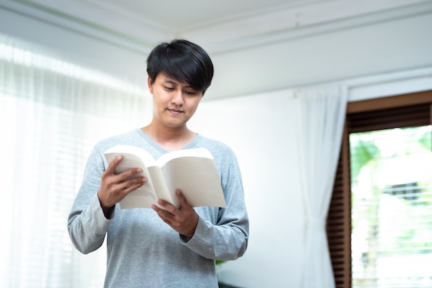 Cheerful asian man dress in casual standing relax in cafe hand hold book look at camera for data research and self improvement.Education and scholarship opportunity.World book day concept.