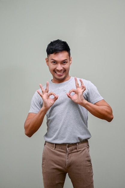 Cheerful Asian man showing OK hand sign while standing against an isolated green background