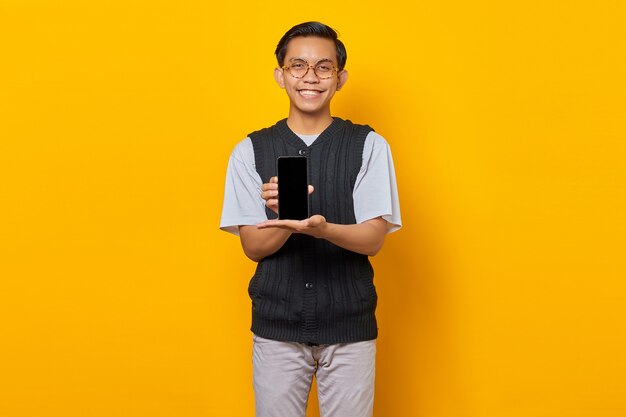 Cheerful Asian man showing smartphone blank screen over yellow background