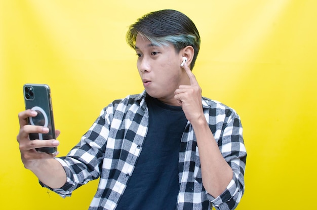 A cheerful Asian man with peek a boo hair uses airpods and looking at phone listening to music