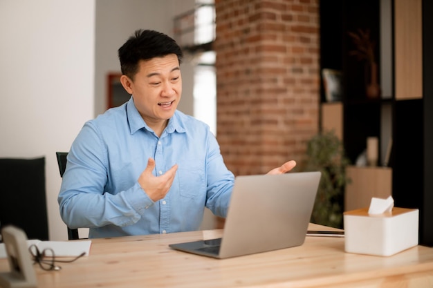 Cheerful asian middle aged man using laptop having video call with colleagues from home while working remotely