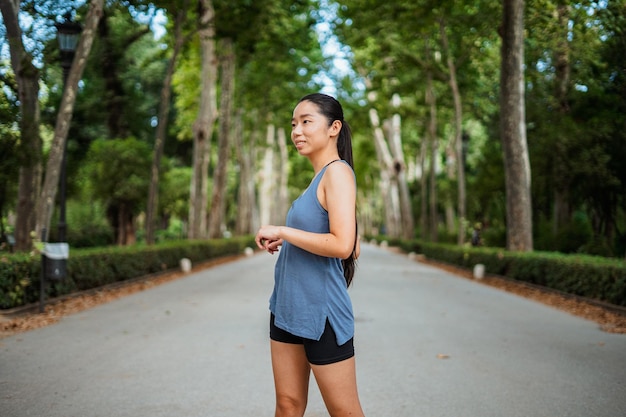 Cheerful asian sport girl warming up in the park before jogging