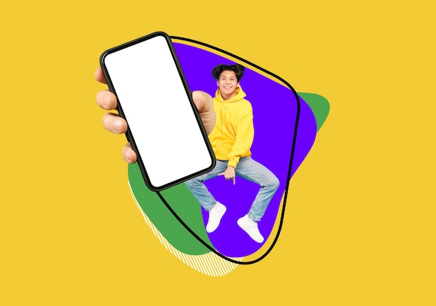 Cheerful asian teen guy jumping up with big blank smartphone in hand