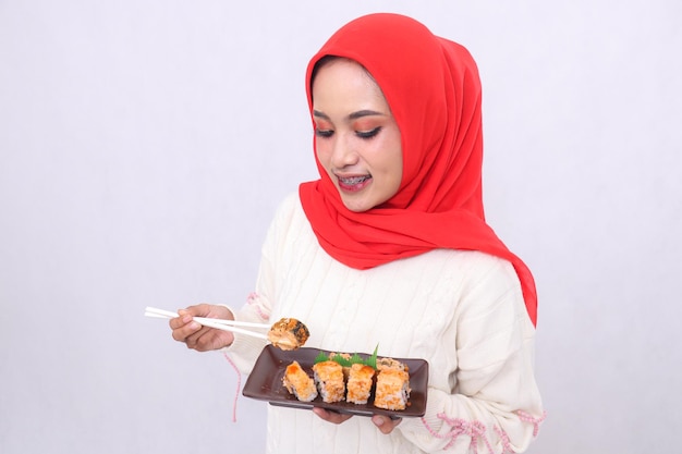 Cheerful Asian woman in hijab top angle candidly holding sushi chopsticks and carrying a plate conta