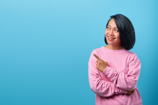 Cheerful Asian woman pointing to empty room on blue background