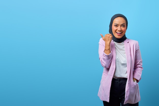 Cheerful Asian woman pointing fingers to empty space over blue background