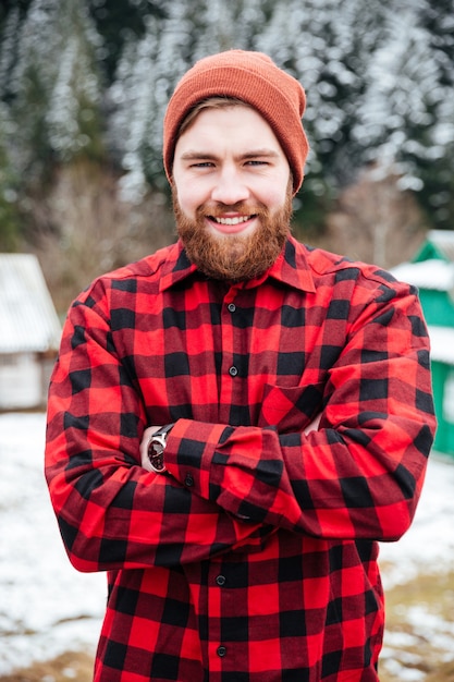 Фото Веселый привлекательный бородатый мужчина, сложив руки в зимней деревне