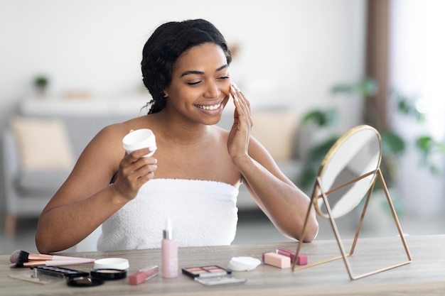 Cheerful attractive black woman using facial cream