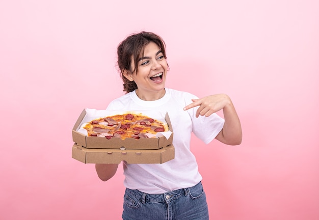 Веселая привлекательная девушка с пиццей в коробке на розовом фоне
