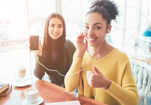 Cheerful and attractive girls are sitting near the bright window in cafe.