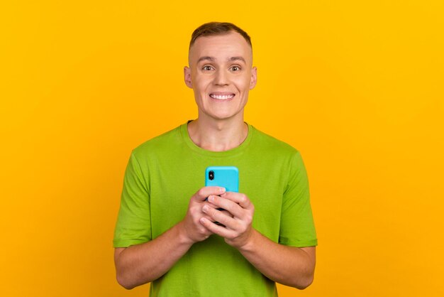 Cheerful attractive guy in casual outfit holding smart phone in hands using 3g internet wifi online shopping over yellow background