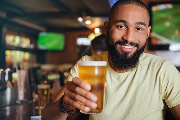 Giovane attraente allegro che beve birra in pub