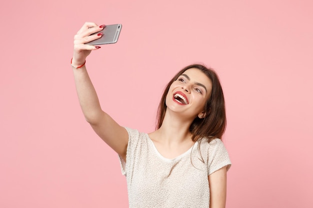 Giovane donna attraente allegra in abiti leggeri casual in posa isolata sul ritratto in studio di sfondo muro rosa pastello. concetto di stile di vita delle persone. mock up spazio di copia. facendo selfie sul cellulare.