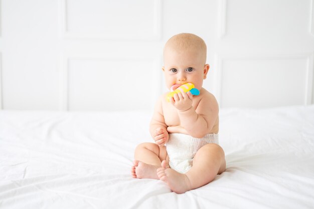 A cheerful baby in a diaper is sitting on a bed the child is holding a toy looking at the camera
