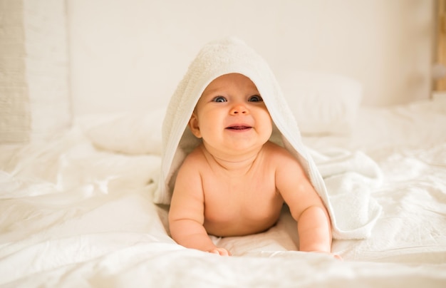 A cheerful baby girl lies in a white bath towel on blanket on the bed