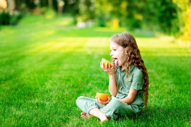 Cheerful baby girl in summer on the lawn with oranges on the green grass having fun and rejoicing space for text