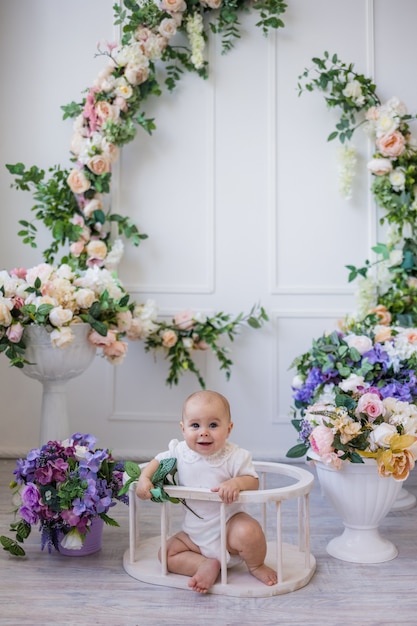 Una bambina allegra in un body bianco è seduta in un'arena su uno sfondo con fiori