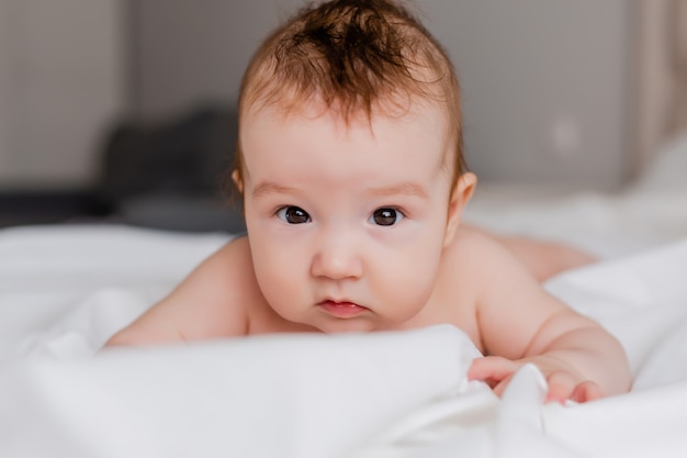 cheerful baby is lying on his stomach on a white bed