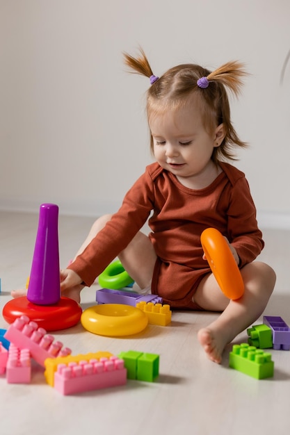 cheerful baby plays with a multicolored pyramid and other educational toys sitting on the floor