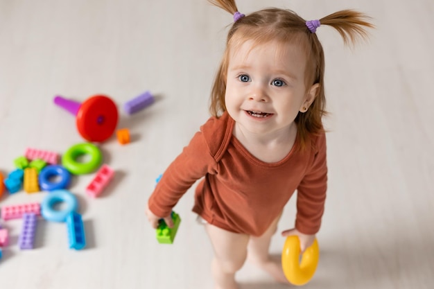 Cheerful baby plays with a multicolored pyramid and other educational toys sitting on the floor