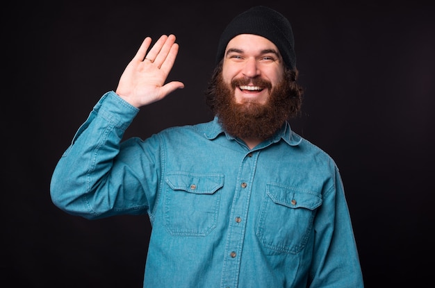 Cheerful bearded hipster man saying hello over dark background