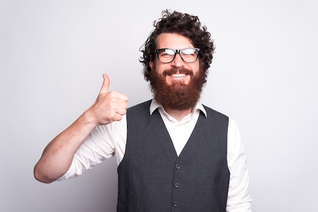 Cheerful bearded hipster man in suit looking confident and showing thumb up