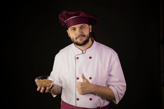 Cheerful bearded male chef in uniform holding bowl of cereal shows thumbs up