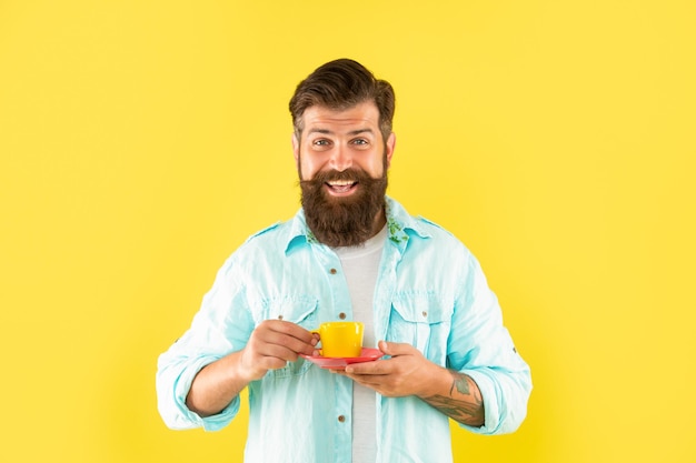 Cheerful bearded man drink morning coffee on yellow background espresso