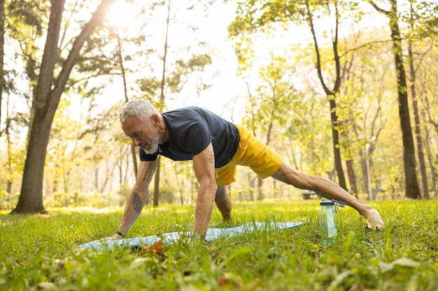 Cheerful bearded man exercising on mat in forest