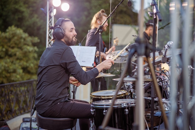 Cheerful bearded man playing drums at outdoor concert