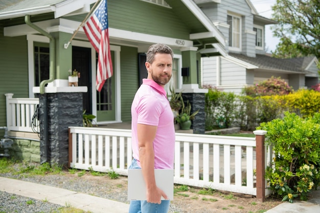 Cheerful bearded man real estate agent selling or renting house online on computer suburb