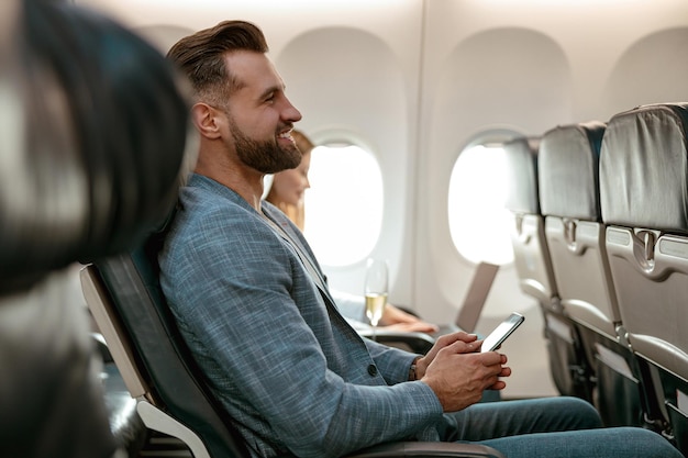 Photo cheerful bearded man using smartphone in airplane