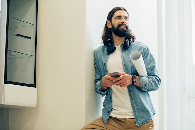 Cheerful bearded young man looking into the distance while holding a smartphone